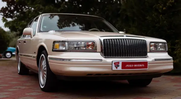 Beżowy Lincoln Town Car, przyszły youngtimer, lśni na tle zieleni. Klasyczna elegancja, która wciąż zachwyca.