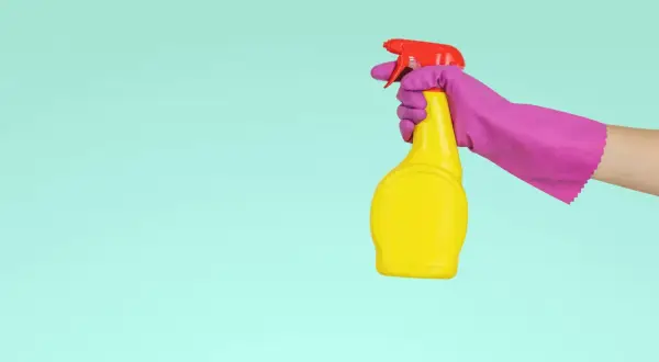 En hand i lila handske håller en gul sprayflaska med röd spraymunstycke, redo för en snabb dry clean.