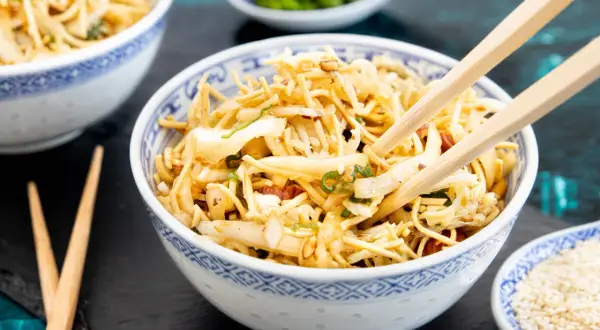 Ein Schüsselchen "friss dich dumm Salat" mit Nudeln, Gemüse und Mandeln, bereit zum Genießen mit Stäbchen.