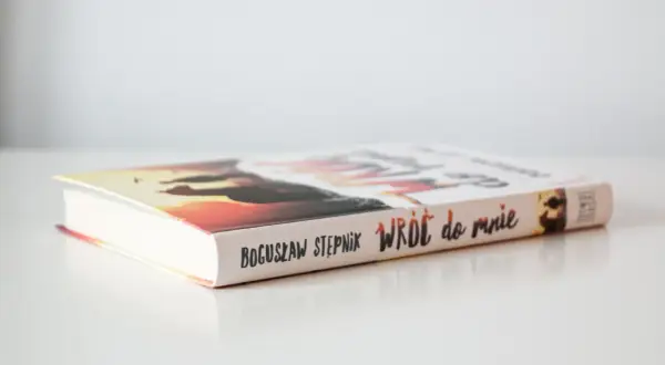 Książka Bogusława Stępnika "Wróć do mnie" na jasnym tle. Okładka z zachodem słońca i sylwetkami.