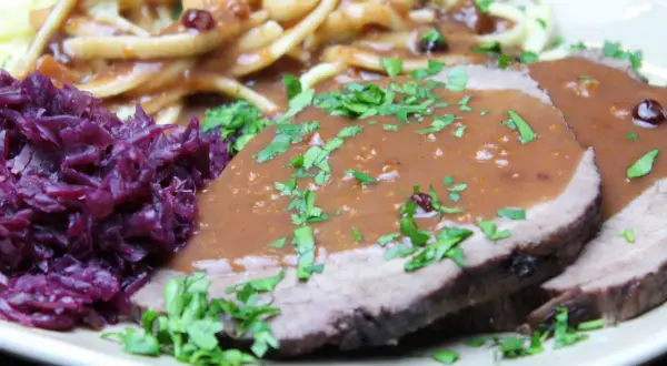 Sauerbraten mit Klößen und Rotkohl. Die Marinierzeit für Sauerbraten kann variieren, oft mehrere Tage.