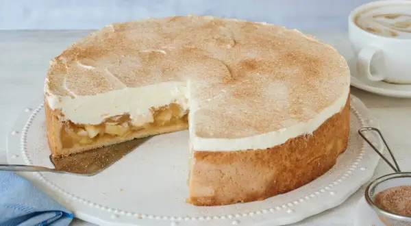Saftige Apfel Schmand Torte mit Zimt bestäubt, bereit zum Servieren neben einer Tasse Kaffee.