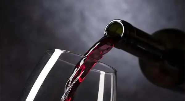Rotwein fließt aus einer Flasche in ein Glas. Eine Frage, die sich viele stellen: ist Wein vegetarisch? Ja, meistens.