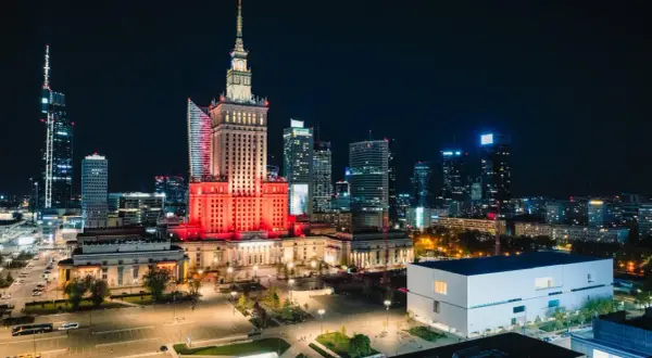 Warszawski Pałac Kultury i Nauki rozświetlony na czerwono, niczym scena przed wielkim koncertem. W tle nocna panorama miasta.