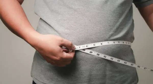 Person misst den Bauchumfang. Viele fragen sich, wo nimmt man zuerst ab – oft ist es der Bauch.