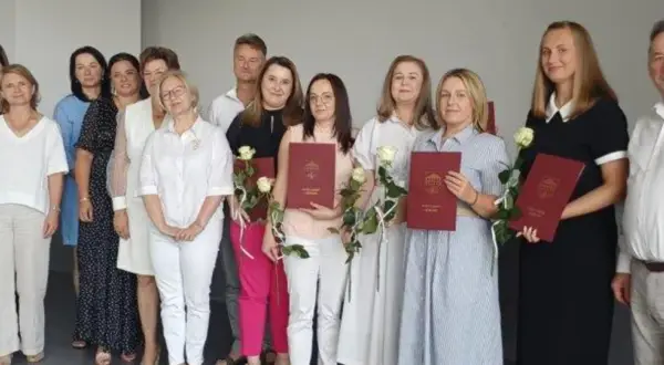 Grupa osób pozuje do zdjęcia, trzymając dyplomy i róże.