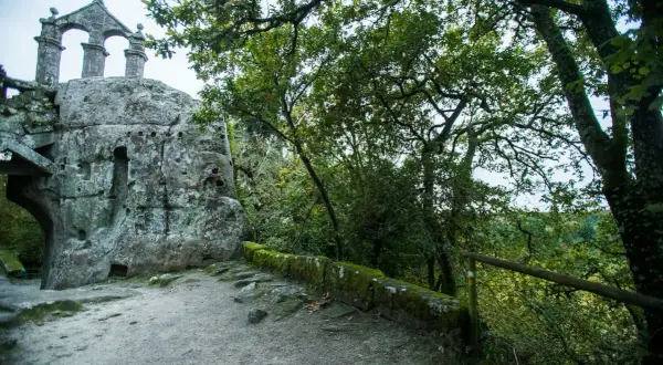 Antigua ermita rupestre de San Pedro de Rocas, con su estructura de piedra y arcos, rodeada de vegetación frondosa.