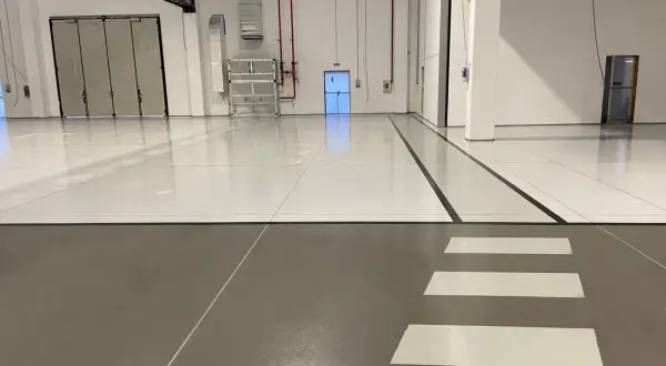 Pavimento industriale con finitura in resina epossidica, segnali di sicurezza e porte a libro.