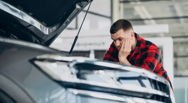 Mężczyzna w kratę sprawdza auto po naprawie bezgotówkowej. Zamyślony, opiera głowę na dłoni.