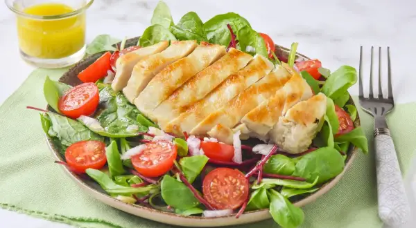 Deliciosa ensalada de pollo a la parrilla con tomates cherry, hojas verdes y aderezo.