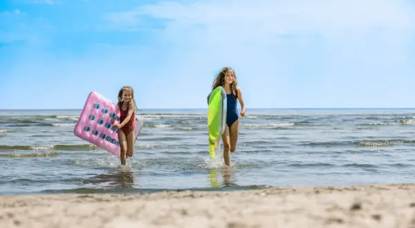 Zwei Mädchen rennen lachend mit Luftmatratzen über den mecklenburgische Seenplatte strand ins Wasser.