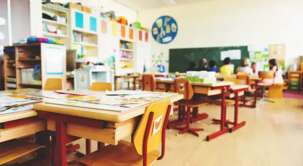 Helle, freundliche klassenraumgestaltung grundschule mit bunten Regalen, kindgerechten Tischen und Stühlen. Kinder sitzen im Hintergrund.