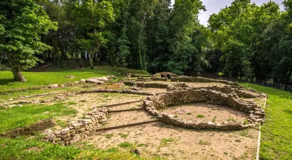 Ruinas de un castro alobre, con muros de piedra y vegetación exuberante.