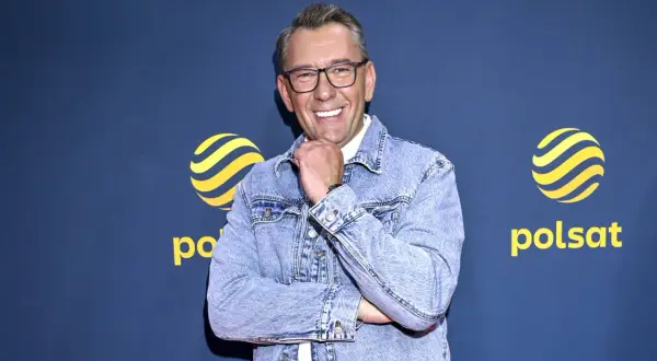 Uśmiechnięty Darek Stolarz w dżinsowej kurtce, z podpartą brodą, na tle logo Polsatu.