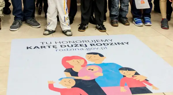 Na macie z napisem "Tu honorujemy Kartę Dużej Rodziny" widnieje rysunek rodziny. Dzieci i dorośli stoją wokół.