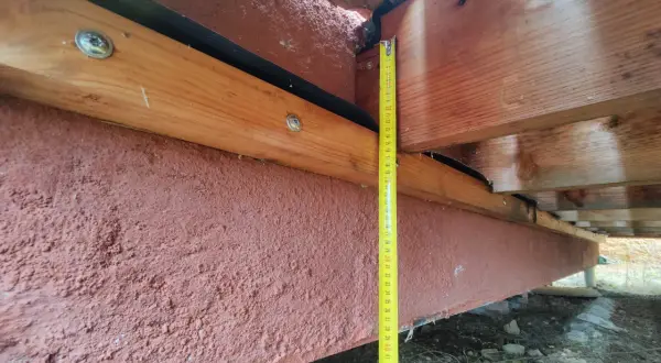 Mesure de la hauteur d'une poutre en bois extérieur, avec un revêtement rouge pour sa protection.