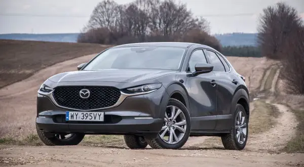 Szary Mazda CX-30 na polnej drodze. Wady tego modelu to m.in. ograniczona widoczność i twarde zawieszenie.
