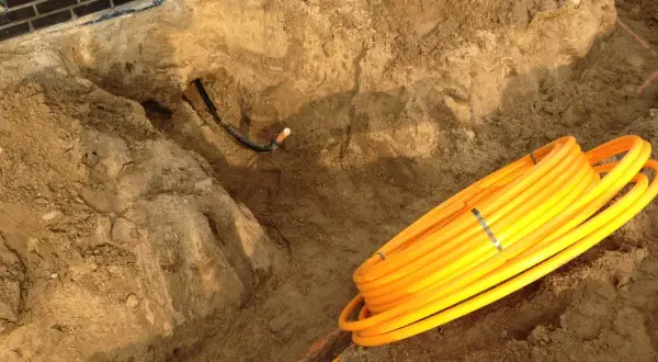 Baustelle: gelbe Rohre liegen bereit für die Gasleitung verlegen im Erdreich. Ein Graben ist ausgehoben.