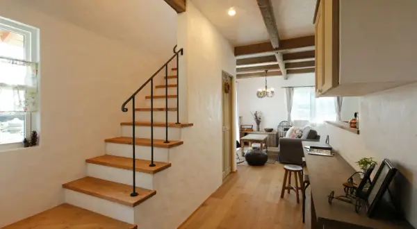 Un acogedor aseo bajo escalera con escalones de madera y barandilla negra. La sala de estar rústica se abre al fondo.