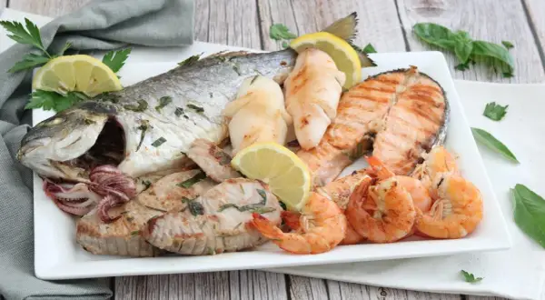 Un piatto invitante di grigliata di pesce: orata intera, tranci di salmone, gamberi, calamari e tonno, guarnito con limone e prezzemolo.
