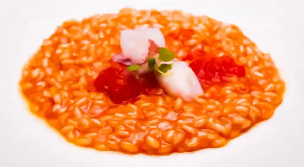 Risotto al porto cremoso con gamberi, pomodorini e un tocco di verde.