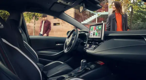 Wnętrze nowoczesnej corolla sedan z ekranem multimedialnym. Na zewnątrz para ludzi.