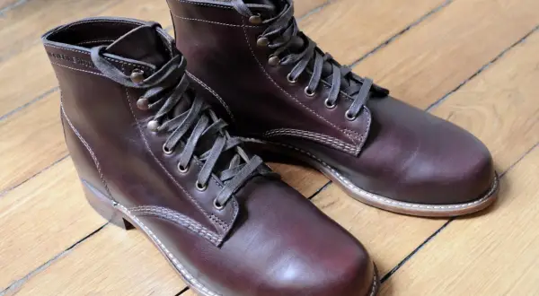 Bottes en cuir brun foncé, parfaites pour reconnaître le cuir gras. Le bois du parquet reflète la lumière sur le cuir.