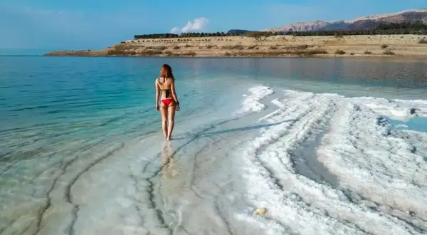 Kobieta w czerwonym bikini stoi na brzegu Morza Martwego, otoczona kryształami soli.