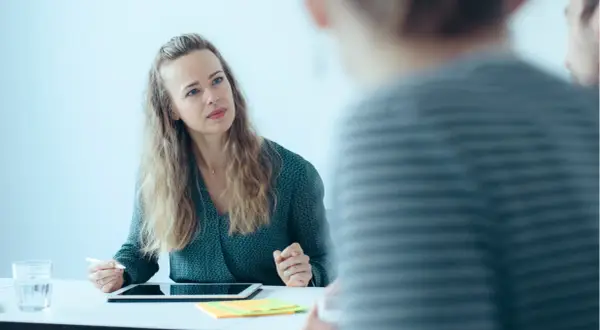 Frau mit Tablet und Stift im Gespräch mit unscharfen Personen.