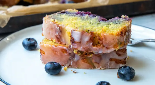 Zwei Scheiben saftiger zitronen blaubeer kuchen mit Zuckerguss und frischen Blaubeeren auf einem Teller.
