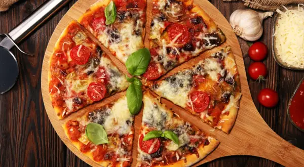 Pyszna pizza z pomidorkami i bazylią, obficie posypana serem do pizzy. Obok czosnek, pomidorki i sos.