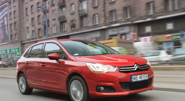 Czerwony Citroen C4 1.6 HDI w ruchu miejskim, z budynkami w tle.
