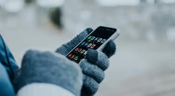 Ręka w rękawiczce trzyma smartfon z ikonami aplikacji. Chcesz wiedzieć, jak sprawdzić czy ktoś jest aktywny na Facebooku?