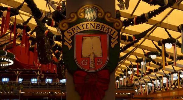 Spatenbräu-Schild mit Schaufel-Symbol, das auf die Herkunft des Bieres hinweist. Festlich geschmückte Halle.