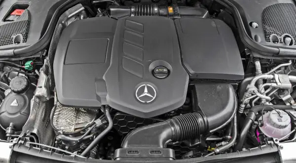 Silnik Mercedes-Benz E-Class. Widoczny czarny plastikowy dyfuzor, logo gwiazdy Mercedesa i elementy układu dolotowego.