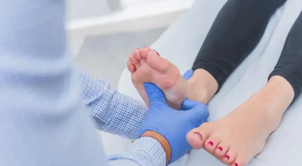 Medico esamina un piede, concentrandosi sulla zona dolente sotto la base delle dita.