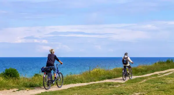 Dwie osoby na rowerach jadą ścieżką wzdłuż morza. To piękny dzień na przejażdżkę szlakiem rowerowym R10 na Mierzei Wiślanej.
