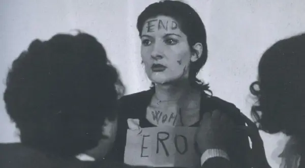 Marina Abramović w performansie "Rhythm 0" z napisem "END" na czole i "WOMAN ERO" na klatce piersiowej.