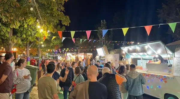 Noche animada en un festival de ebro food trucks, con luces, banderas y gente disfrutando.