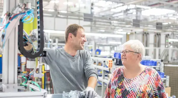 Zwei Kollegen in einer Fabrikhalle, die über ihre Arbeit sprechen. Vielleicht diskutieren sie, wie wird man Betriebsrat, um die Arbeitsbedingungen zu verbessern.