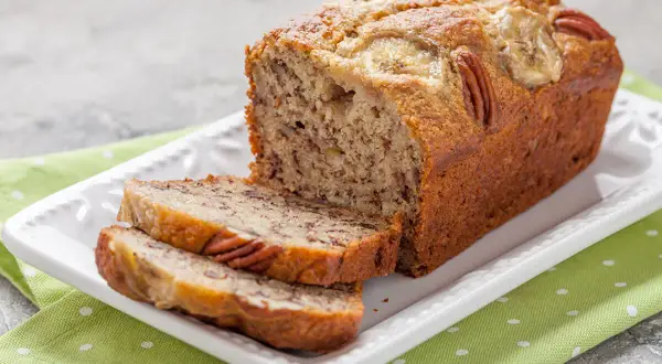 Pyszny chlebek bananowy fit z orzechami pekan i plasterkami banana na wierzchu, pokrojony na talerzu.