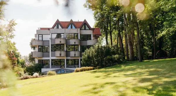 Hotelgebäude mit Balkonen und Spitzdächern, umgeben von Bäumen und einer grünen Wiese.