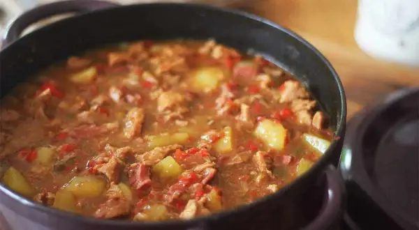 Un plat mijoté d'axoa de veau avec des pommes de terre et des poivrons rouges, servi dans une cocotte.