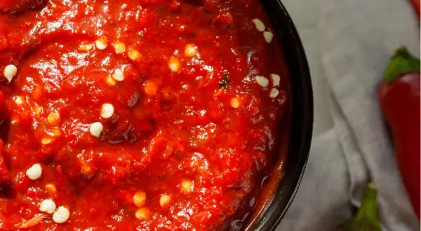 Nahaufnahme einer Schüssel mit leuchtend roter Harissa-Paste, gesprenkelt mit weißen Chiliflocken. Ein einfaches harissa rezept.