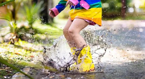 Bambino con stivali gialli salta in una pozzanghera, creando spruzzi d'acqua. Ecco perché i bambini si sdraiano per terra: per godersi il gioco!