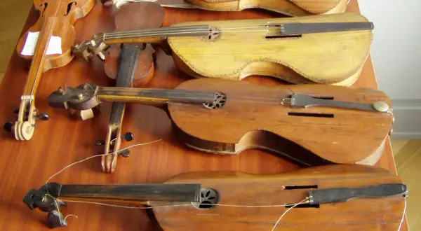Na stole leży kilka instrumentów smyczkowych. Jeden z nich to pudło skrzypiec, które wygląda na bardzo stare.