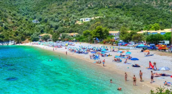 Piękna plaża z turkusową wodą, zielone wzgórza i domki w tle. To idealne miejsce na wakacje na Karaibach, wyspy zapraszają do odpoczynku.
