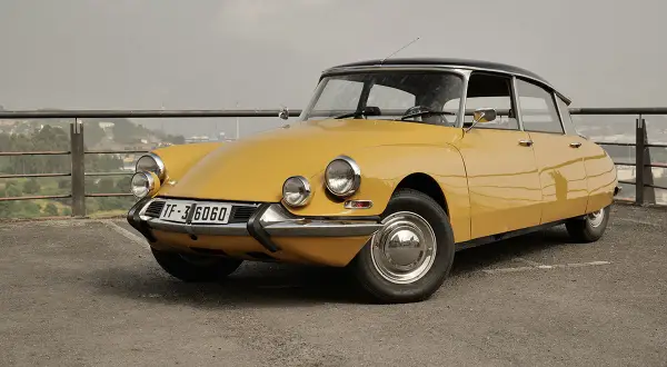 Citroën Tiburón amarillo, un clásico icónico con su diseño aerodinámico y faros distintivos, aparcado en un mirador con vistas a la ciudad.