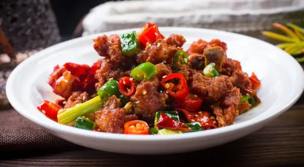 Chrupiący kurczak po kantońsku z papryczkami chili i zieloną cebulką na białym talerzu.