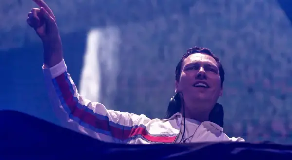 DJ Tiësto wznosi rękę, wskazując na tłum podczas jednego ze swoich energetycznych koncertów.